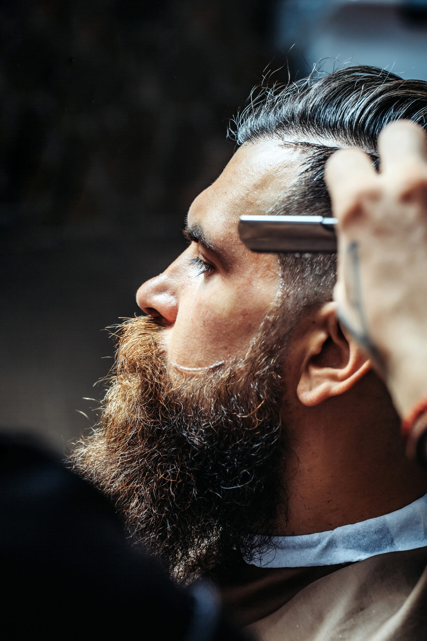 Bearded man with long beard getting hair shaving with razor