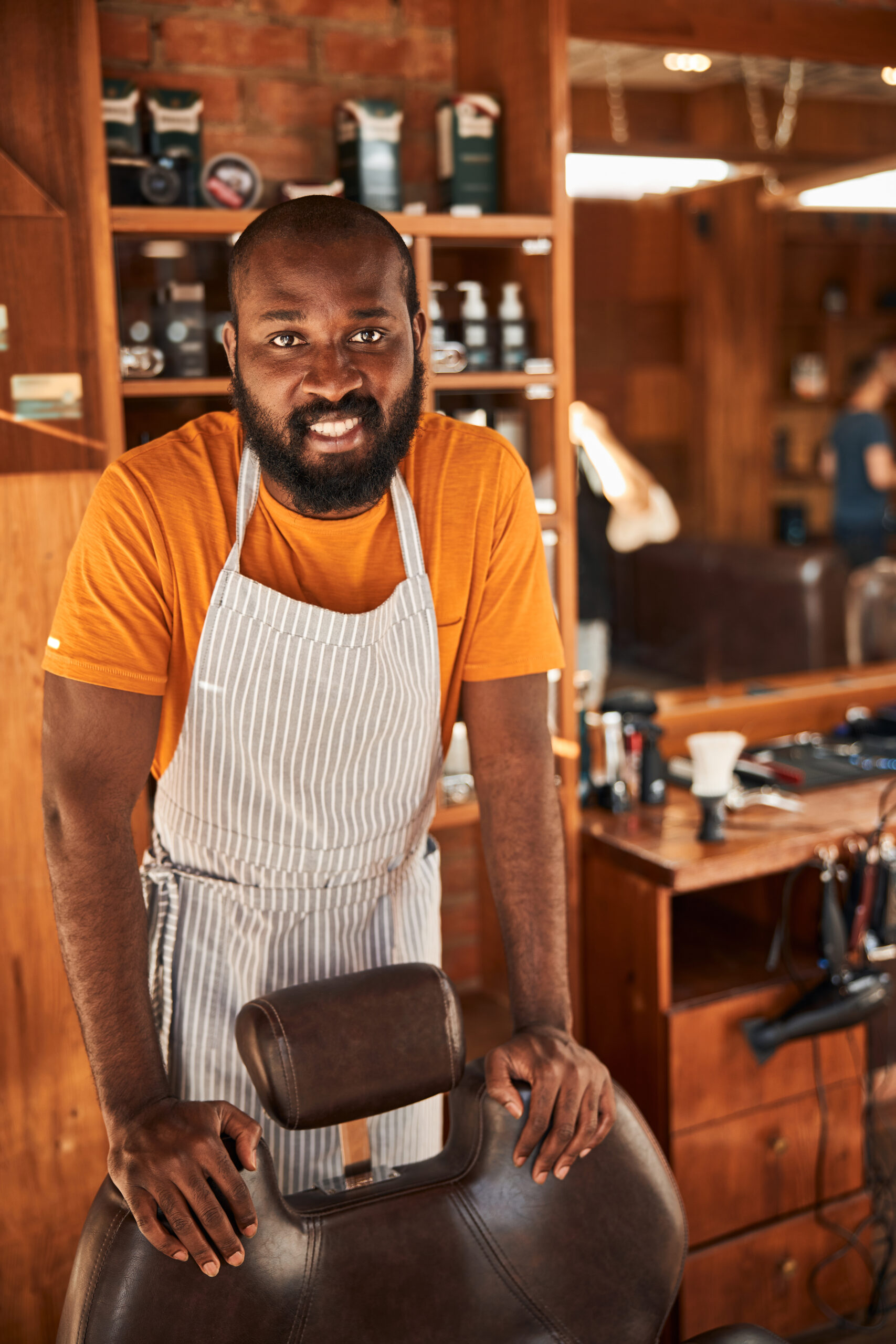 Joyful male barber in apron standing in barbershop